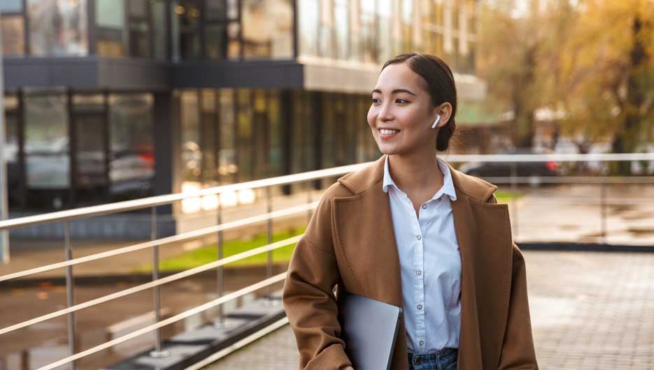 Image of young brunette asian woman holding laptop while walking