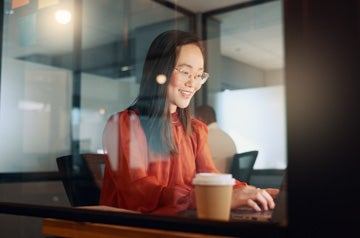 Laptop, night office and Asian woman typing email, sales proposal or finishing project deadline. Computer, tech and happy female employee working late in dark workplace, researching or writing report.