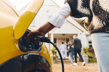 Woman plugging electric charger into car outside Home With Family