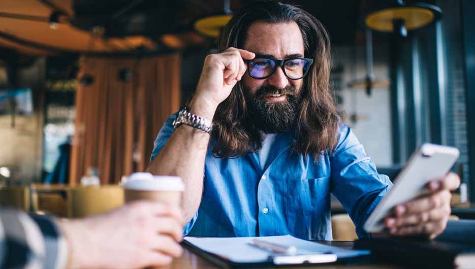 Positive bearded caucasian male using mobile phone for checking 